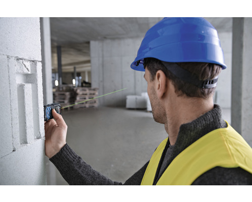 Un homme portant un casque de protection et un gilet de sécurité utilise un télémètre laser sur un chantier de construction.