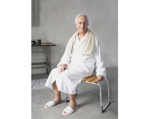 Ein Mann im Bademantel sitzt auf einem Duschhocker mit Holzlatten und Metallrahmen.