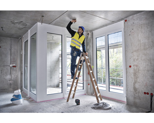 Innenraumszene im Rohbau mit Handwerker auf einer Leiter bei der Arbeit an der Decke.