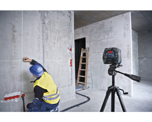 Ein Arbeiter markiert mit einem Kreuzlinienlaser Punkte an einer Betonwand in einem Rohbau.