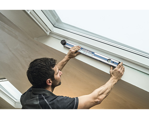 Ein Mann benutzt eine digitale Wasserwaage an einem Dachfenster.