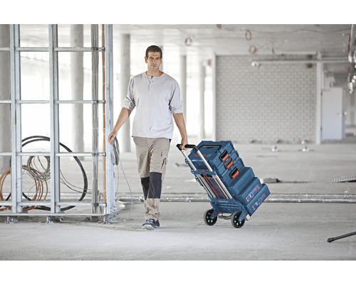 Un artisan tire un chariot de caisses à outils Bosch sur un chantier.