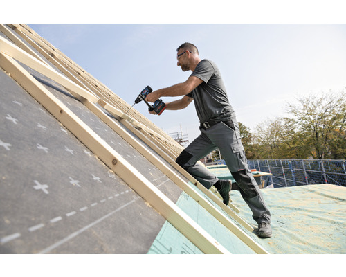 Ein Handwerker befestigt Dachlatten mit einem Akku-Bohrschrauber auf einer Dachkonstruktion.