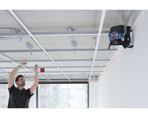 Un homme installe une structure de plafond avec un laser lignes croisées pour l'alignement