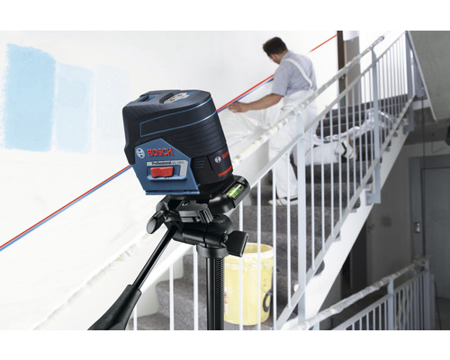 Logo Bosch. Niveau laser croix sur trépied avec artisan dans la cage d'escalier.