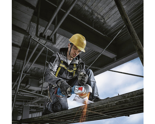 Mann mit Schutzhelm und Winkelschleifer beim Metallschneiden auf einer Baustelle