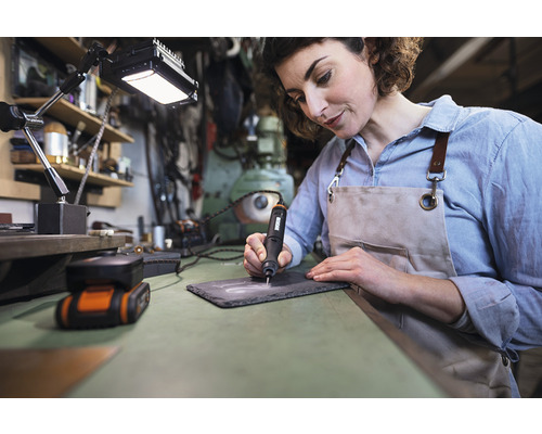 Une femme grave une plaque d''ardoise avec une graveuse sur un établi.