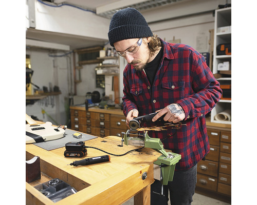 Un homme travaille avec une meuleuse d''angle sur une pièce fixée dans un étau sur un établi. On aperçoit également un outil multifonction et une batterie.