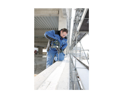 Un homme perce une poutre en béton avec une perceuse Metabo sur un échafaudage.