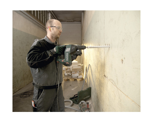 Un homme perce un trou dans un mur avec un marteau perforateur Metabo.