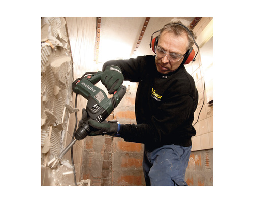 Un homme portant des lunettes de protection et un casque antibruit enlève des carreaux du mur avec un perforateur burineur Metabo.