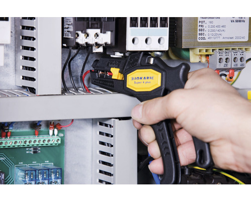 Une personne utilise une pince à dénuder Jokari Super 4 Plus sur un boîtier électrique.