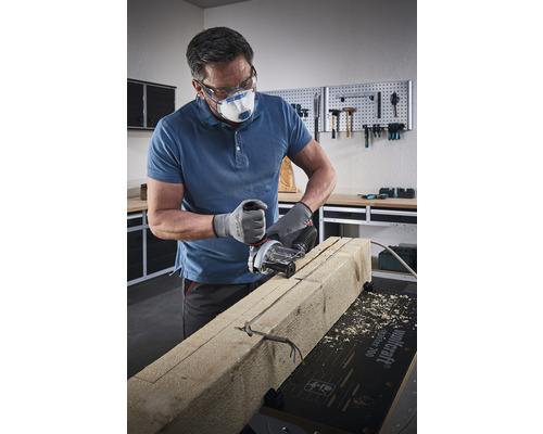 Un artisan portant des lunettes de protection et un masque respiratoire découpe une pièce de bois à la scie à rainurer.