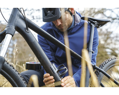 Un homme fixe un porte-bidon à un vélo avec du ruban adhésif.