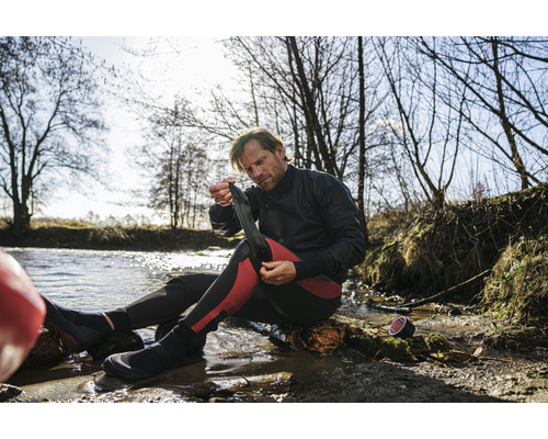Un homme enfile des chaussettes en néoprène au bord de l''eau