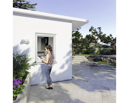 Une femme se tient devant une cabane de jardin avec une fenêtre en plastique et profite de la vue sur le jardin.
