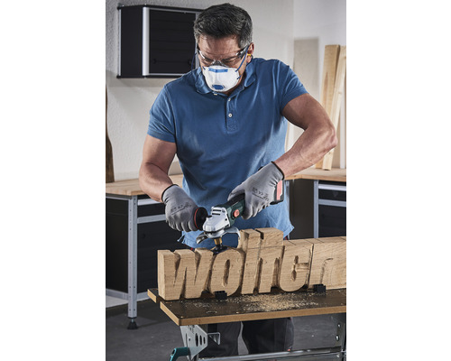 Ein Mann formt mit einer Holzfrässcheibe den Schriftzug Holz.