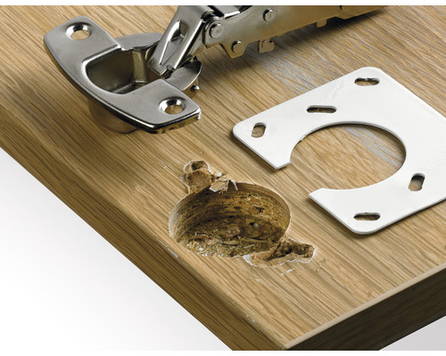 Möbelscharnier mit Montageplatte auf einer Holzoberfläche und Bohrloch