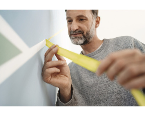 Mann klebt Malerkrepp an Wand mit Farbdesign.