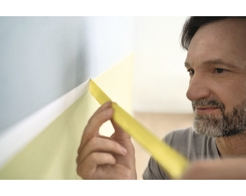 Mann klebt Malerkrepp an eine Wand für Farbarbeiten