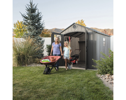 Szene mit einer Mutter, einem Kind, einem Geräteschuppen, einer Schubkarre und Gartengeräten in einem Garten.