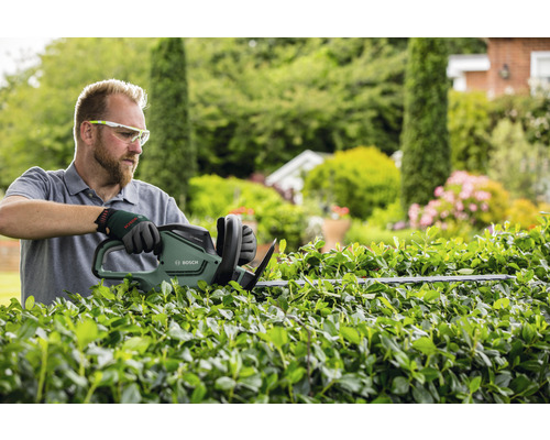 Un homme taille une haie avec un taille-haie Bosch dans le jardin.