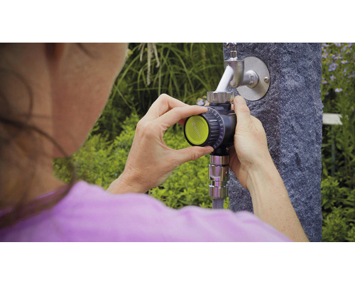 Frau bedient einen Bewässerungscomputer am Wasserhahn im Garten.