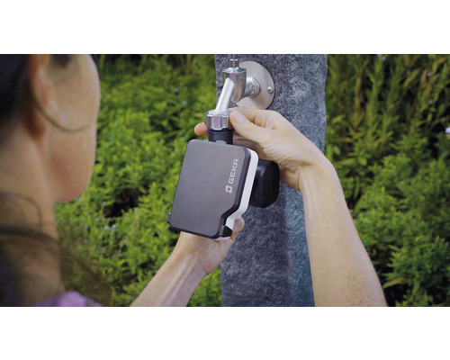 Eine Person befestigt eine Geka Bewässerungssteuerung an einem Wasserhahn im Garten.