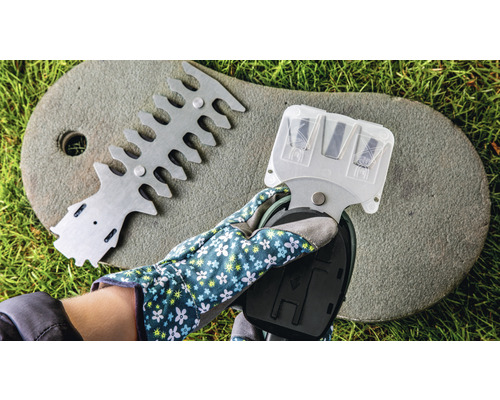 Eine Hand mit Gartenhandschuh hält ein Heckenscheren-Schärfgerät, neben einer Vorrichtung zum Ausrichten von Heckenscheren