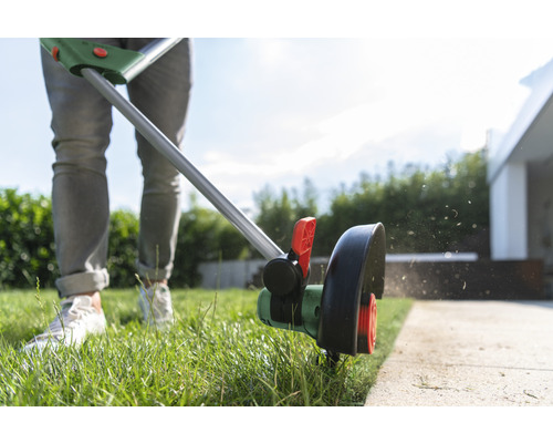 Person trimmt Rasen mit Rasentrimmer am Gartenweg