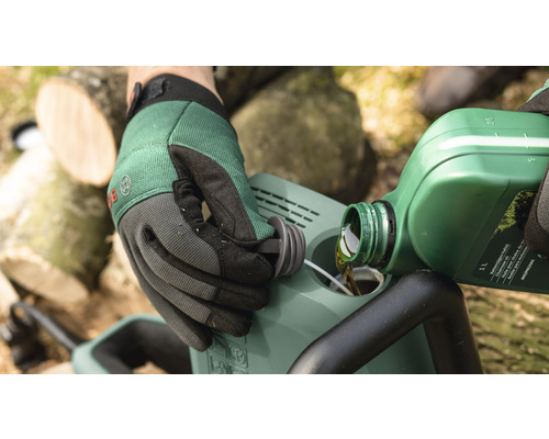 Une personne verse de l''huile de chaîne dans une tronçonneuse. Des gants sont portés.