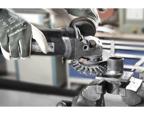 Eine Person verwendet eine Drahtbürste an einem Winkelschleifer, um ein Metallstück in einem Schraubstock zu bearbeiten. Dabei trägt die Person Schutzhandschuhe.