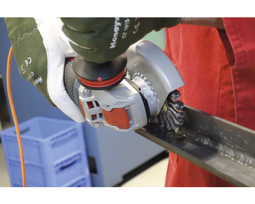 Arbeiter benutzt eine Drahtbürste an einem Winkelschleifer, um ein Metallstück zu reinigen