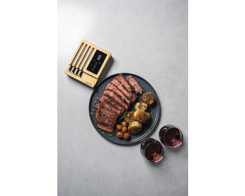 Ein Teller mit geschnittenem Steak, Kartoffeln, Tomaten, zwei Gläsern Wein und einem Fleischthermometer