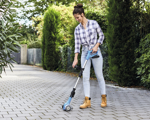 Frau benutzt eine Fugenbürste zur Reinigung eines Steinwegs.