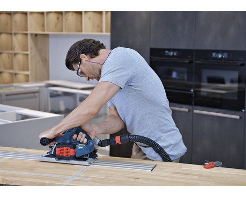 Mann sägt Holzplatte mit Tauchsäge in Werkstatt