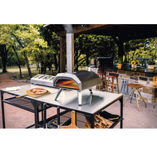 Four à pizza Ooni sur une table avec pizza, ingrédients et bois