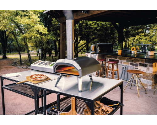 Four à pizza Ooni sur une table avec pizza, ingrédients et bois