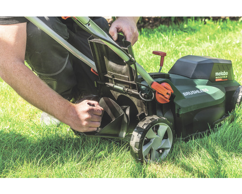 Une personne vide le bac de ramassage d''une tondeuse à gazon sans fil Metabo sur une pelouse.