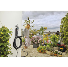 Une femme arrose des plantes sur le balcon avec un tuyau d''arrosage fixé à un support mural