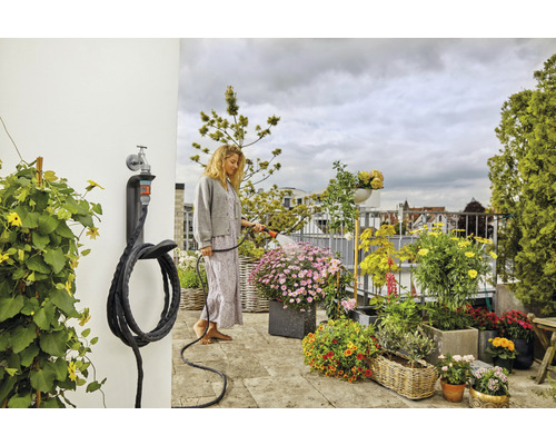 Une femme arrose des plantes sur le balcon avec un tuyau d''arrosage fixé à un support mural