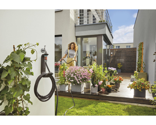 Frau giesst Blumen mit einem Gartenschlauch im Garten mit Schlauchhalterung