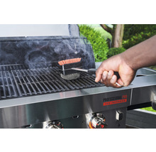 Une personne nettoie un barbecue avec une brosse de barbecue.