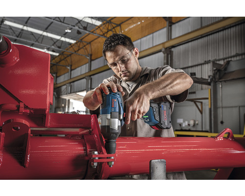 Mann arbeitet mit einem Akku-Drehschlagschrauber an einer roten Metallkonstruktion.