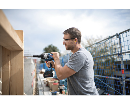 Mann mit Schutzbrille, Gehörschutz und Akku-Schlagschrauber bei der Arbeit an einer Holzkonstruktion