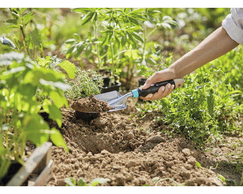 Jardinier plantant des semis en terre avec une plantoir.