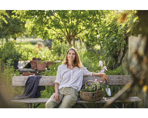Femme assise sur un banc dans le jardin avec un panier de fleurs et un outil de jardinage