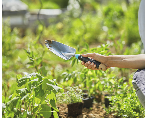 Une personne tient une plantoir Gardena dans le jardin.