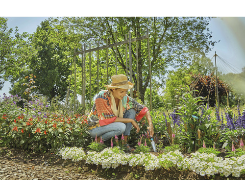 Eine Frau mit Hut arbeitet im Garten zwischen Blumen und Pflanzen.