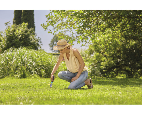 Eine Frau arbeitet mit einem Unkrautstecher im Garten.